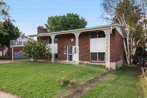 Bi-level home with a front yard, brick siding, a chimney, and a porch