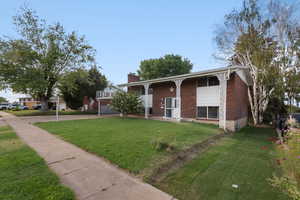 Split foyer home with brick siding, a front yard, driveway, and a chimney