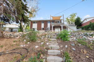 View of front of property with stairs, brick siding, and a patio