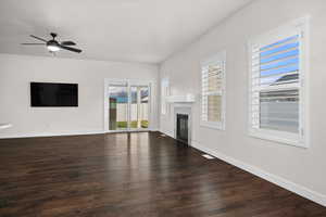 Unfurnished living room featuring dark wood-style floors, a glass covered fireplace, and a ceiling fan