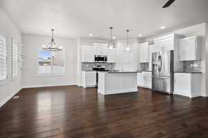 Kitchen with a chandelier, stainless steel appliances, hanging light fixtures, dark countertops, and white cabinets