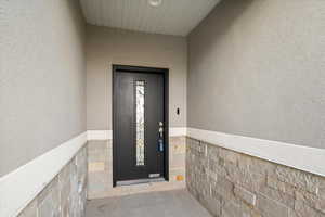 Doorway to property featuring stucco siding and stone siding
