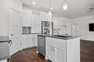 Kitchen featuring stainless steel appliances, an island with sink, white cabinets, dark wood-type flooring, and pendant lighting