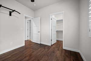 Unfurnished bedroom featuring a walk in closet, dark wood finished floors, and a ceiling fan