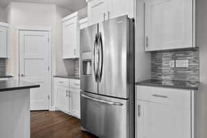 Kitchen with tasteful backsplash, stainless steel refrigerator with ice dispenser, dark wood-style floors, and white cabinets