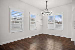 Unfurnished dining area featuring dark wood finished floors, healthy amount of natural light, and a chandelier