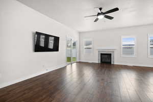 Unfurnished living room featuring a glass covered fireplace, a ceiling fan, and dark wood-style floors