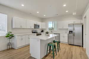 Kitchen featuring stainless steel appliances, a breakfast bar, white cabinetry, a kitchen island, and light wood finished floors