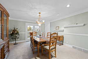 Dining room with light colored carpet, crown molding, and a chandelier
