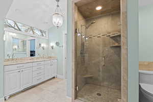 Full bath featuring a chandelier, double vanity, a stall shower, and lofted ceiling
