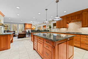 Kitchen with dark stone countertops, brown cabinets, light tile patterned floors, open floor plan, and a kitchen island