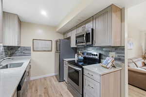 Kitchen featuring appliances with stainless steel finishes, light stone countertops, and tasteful backsplash