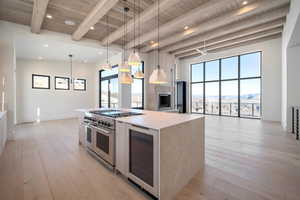 Kitchen with pendant lighting, double oven range, wine cooler, light wood-type flooring, and a wood ceiling with exposed beams