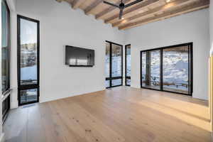 Unfurnished living room featuring a wood ceiling with exposed beams, healthy amount of natural light, a ceiling fan, and light wood-style floors