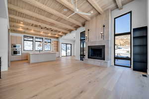 Unfurnished living room with a fireplace, light wood-style floors, ceiling fan, a wooden ceiling with exposed beams, and a towering ceiling