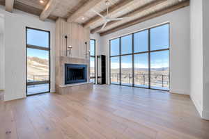 Unfurnished living room featuring a mountain view, a tile fireplace, light wood finished floors, a ceiling fan, and a wood ceiling with exposed beams