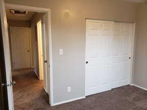 Unfurnished bedroom with dark colored carpet, a closet, and cooling unit