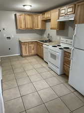 Kitchen featuring white appliances, light countertops, light tile patterned flooring, and under cabinet range hood