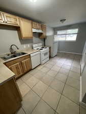Kitchen with white appliances, light countertops, light tile patterned floors, and under cabinet range hood