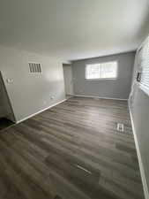 Unfurnished living room with dark wood-style flooring and baseboards