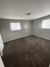 Unfurnished room featuring healthy amount of natural light and dark colored carpet