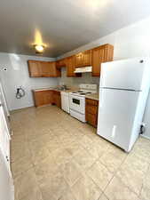 Kitchen featuring white appliances, light countertops, under cabinet range hood, and brown cabinets