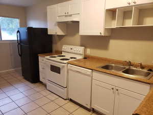 Kitchen featuring white appliances, white cabinets, under cabinet range hood, light tile patterned floors, and light countertops