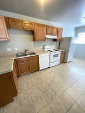 Kitchen featuring white appliances, light countertops, brown cabinets, and under cabinet range hood