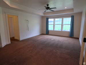 Carpeted empty room with a raised ceiling, recessed lighting, and a ceiling fan