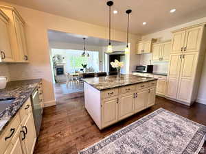 Kitchen featuring cream cabinetry, hanging light fixtures, a kitchen island, dark wood-type flooring, and dark stone countertops