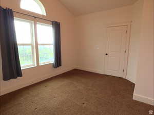 Unfurnished room featuring lofted ceiling and dark carpet