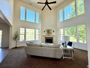 Living area with a towering ceiling, a fireplace, dark colored carpet, and plenty of natural light