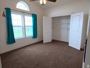 Unfurnished bedroom with dark carpet, lofted ceiling, and ceiling fan