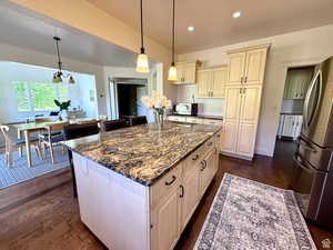 Kitchen with freestanding refrigerator, dark stone counters, pendant lighting, cream cabinets, and recessed lighting