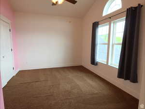 Carpeted spare room featuring vaulted ceiling and a ceiling fan