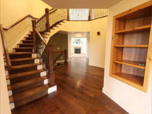 Stairs with built in features, a fireplace with raised hearth, hardwood / wood-style floors, and a towering ceiling