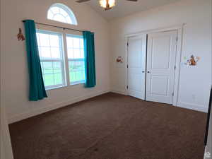Unfurnished bedroom featuring vaulted ceiling, dark colored carpet, a ceiling fan, and a closet