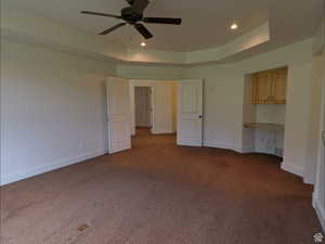 Unfurnished bedroom featuring built in desk, a raised ceiling, dark colored carpet, ceiling fan, and recessed lighting