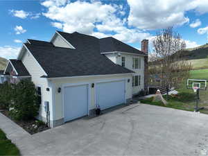 View of property exterior with driveway, a shingled roof, a chimney, and an attached garage