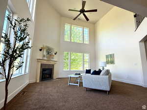 Living area featuring a high ceiling, a high end fireplace, dark colored carpet, and a ceiling fan