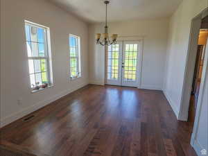 Unfurnished dining area featuring dark wood-style floors, a chandelier, and french doors