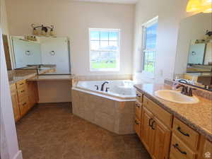 Bathroom featuring a jetted tub, two vanities, and dark tile patterned flooring