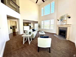 Living area with high vaulted ceiling, a ceiling fan, a fireplace with flush hearth, and dark colored carpet
