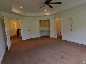 Unfurnished bedroom with built in study area, a raised ceiling, dark colored carpet, ceiling fan, and recessed lighting