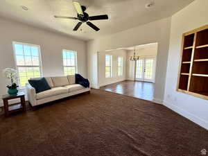 Living room with a ceiling fan, dark colored carpet, a chandelier, french doors, and a textured ceiling