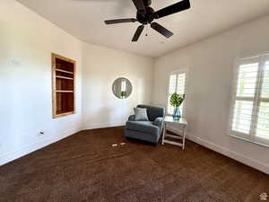 Living area featuring built in shelves, dark colored carpet, and a ceiling fan