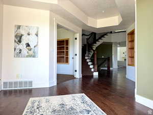 Foyer featuring dark wood-style floors, a textured ceiling, stairway, and a raised ceiling