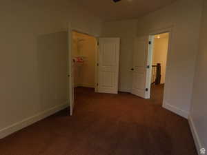 Unfurnished bedroom featuring a walk in closet and dark carpet