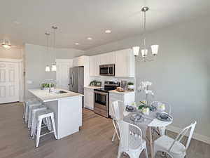 Kitchen featuring white cabinetry, stainless steel appliances, a kitchen bar, light wood-style flooring, and a chandelier