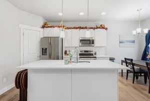 Kitchen with white cabinetry, appliances with stainless steel finishes, a center island with sink, backsplash, and decorative light fixtures